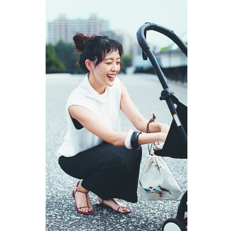 スカートを穿いた古谷有美さんがベビーカーの赤ちゃんに向けて微笑む様子