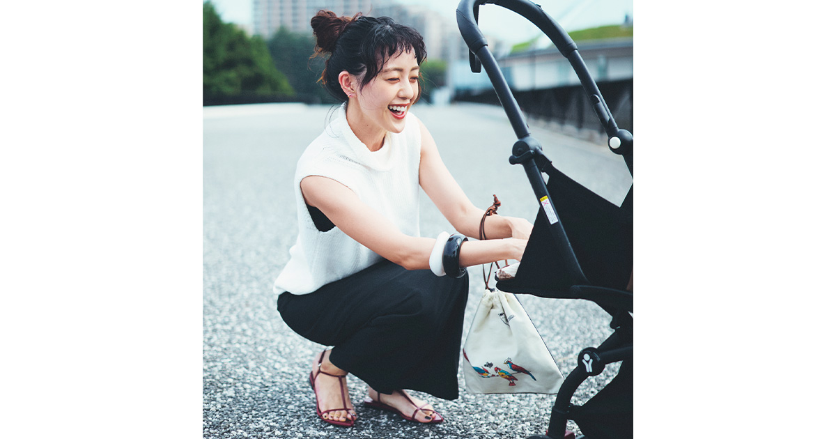 スカートを穿いた古谷有美さんがベビーカーの赤ちゃんに向けて微笑む様子