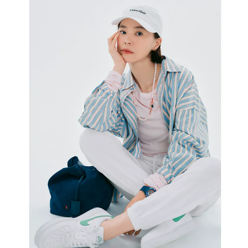 ピンクのシャツにストライプシャツ、キャップのコーデ