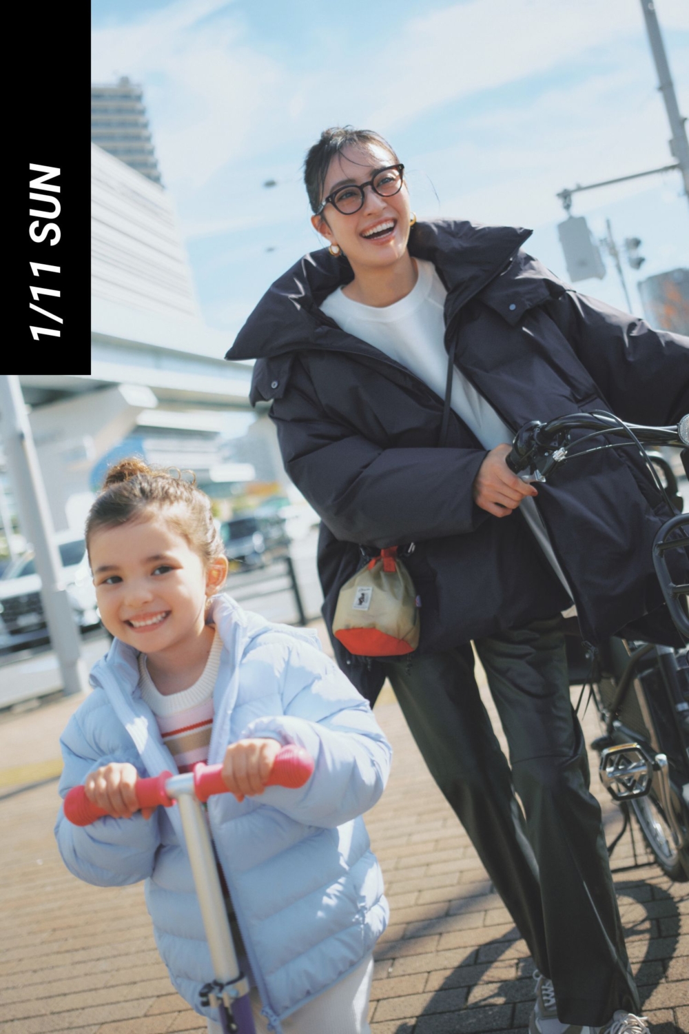 裾広がりの黒ダウンとエコレザーパンツをはいて自転車を押すママ
