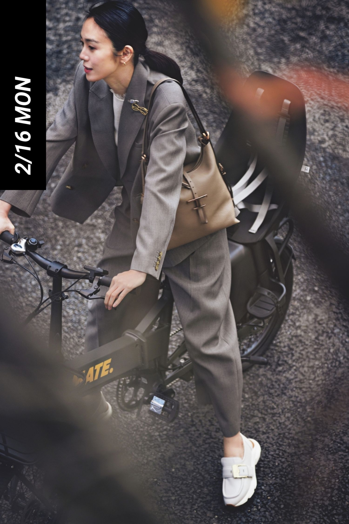 スーツにスニーカーローファーを履いて自転車にまたがるママ