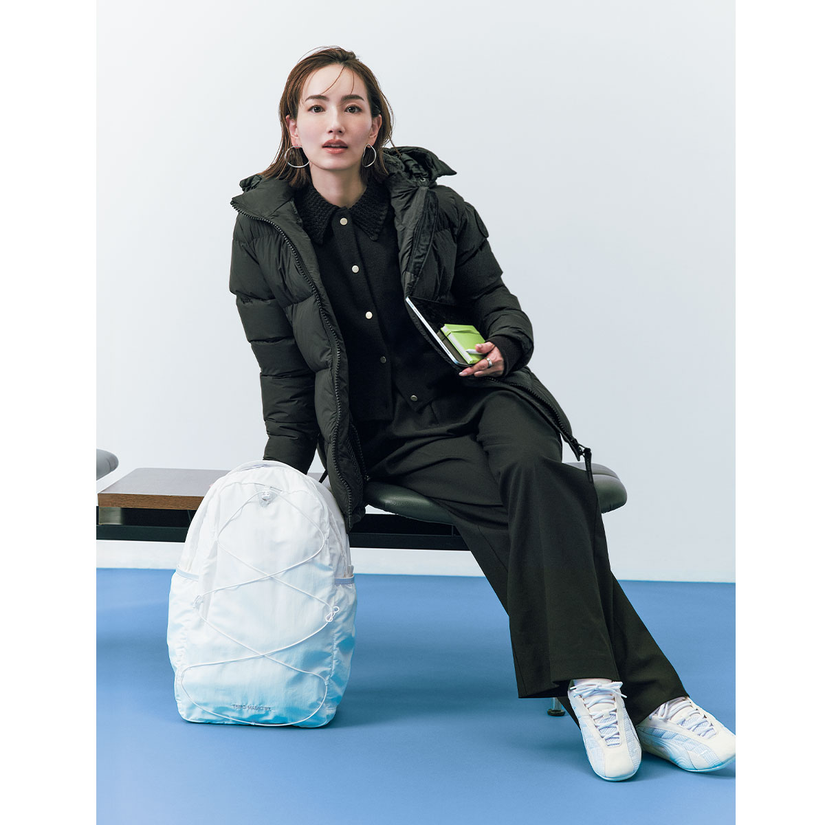 カーディガンとパンツにダウンを羽織ったオール黒コーデに白のリュックとスニーカーを合わせたコーデ