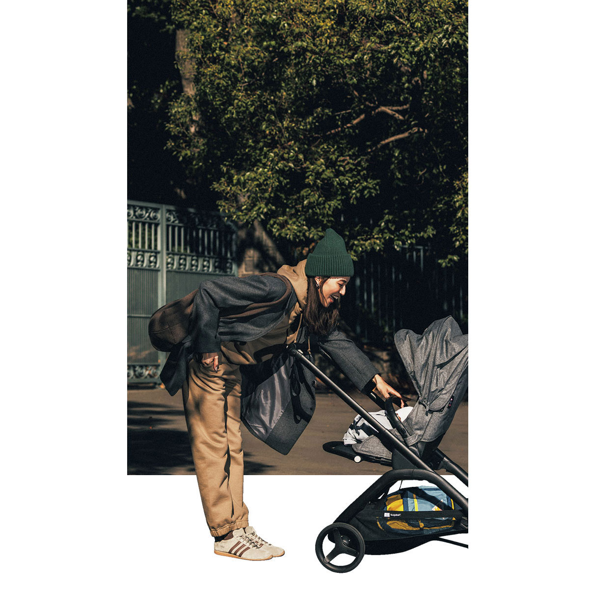 リラクシーなキャメルベージュのフーディセットアップでベビーカーの子どもに笑いかけるママ