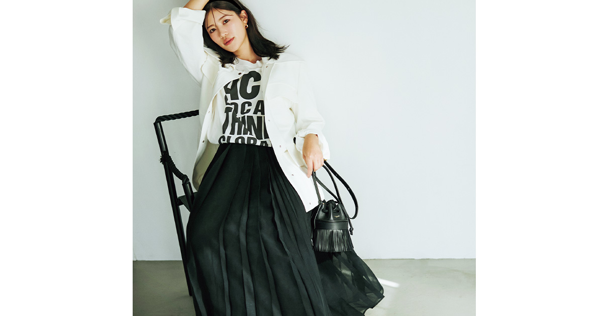 ロゴTシャツと黒のフレアスカートに白のシャツジャケットを羽織ったコーデ