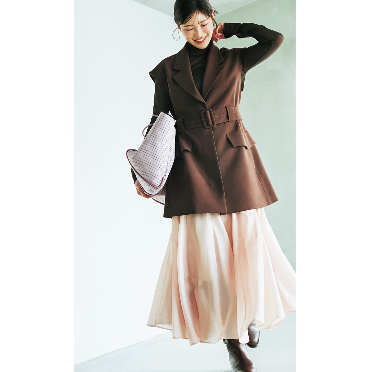 タートルトップスとフレアスカートにベルトマークしたジレを重ねたコーデ