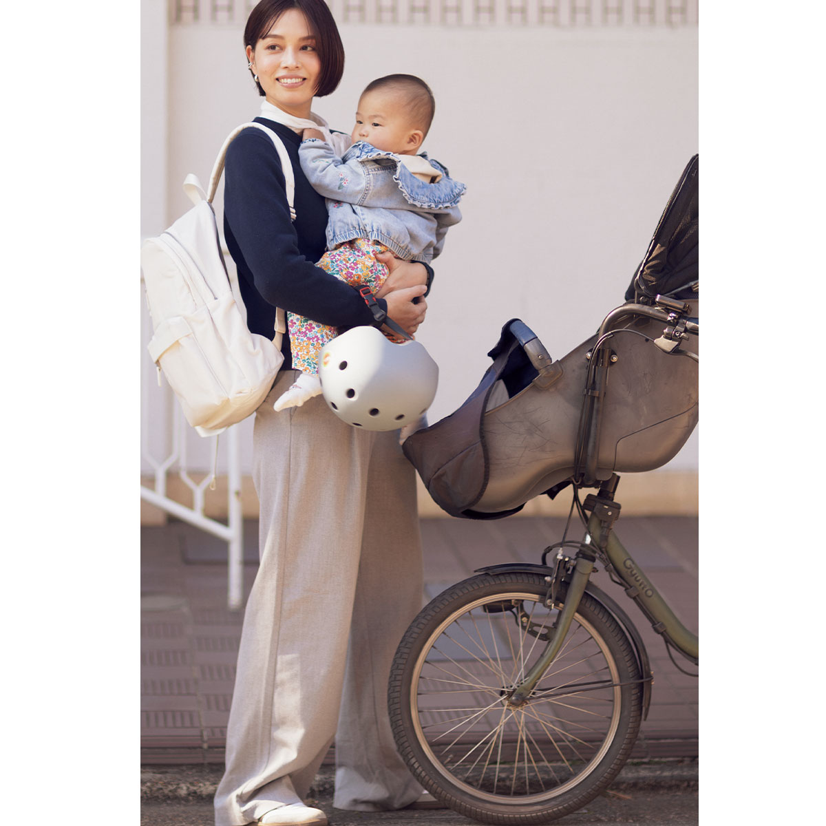リュックにパンツスタイルで赤ちゃんを抱っこする自転車通勤ママ