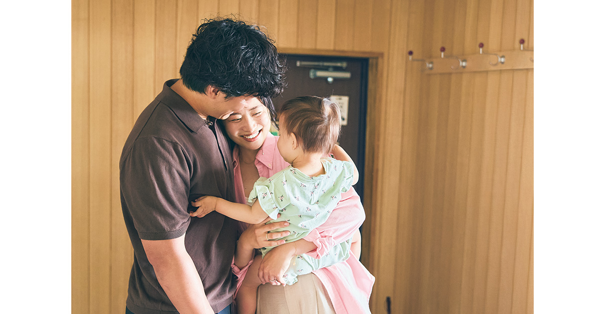 玄関でハグするご夫婦と1歳の娘さん