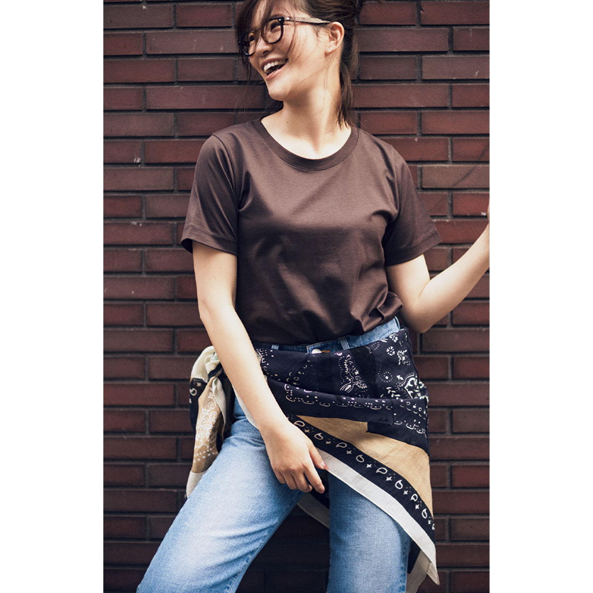 ブラウンの半袖Tシャツにデニム、腰巻きした柄スカーフのコーデ